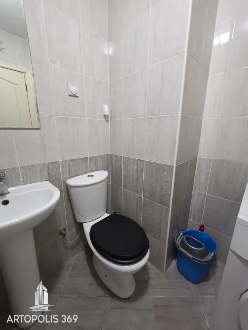 Manje kupatilo sa umivaonikom, šoljom i pločicama u sivoj boji.