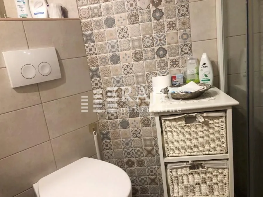View of the bathroom with a toilet and a chest of drawers with wicker baskets.