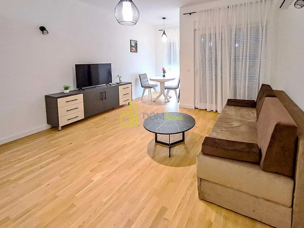 Spacious living room with a sofa, TV cabinet, and a dining area in the background.