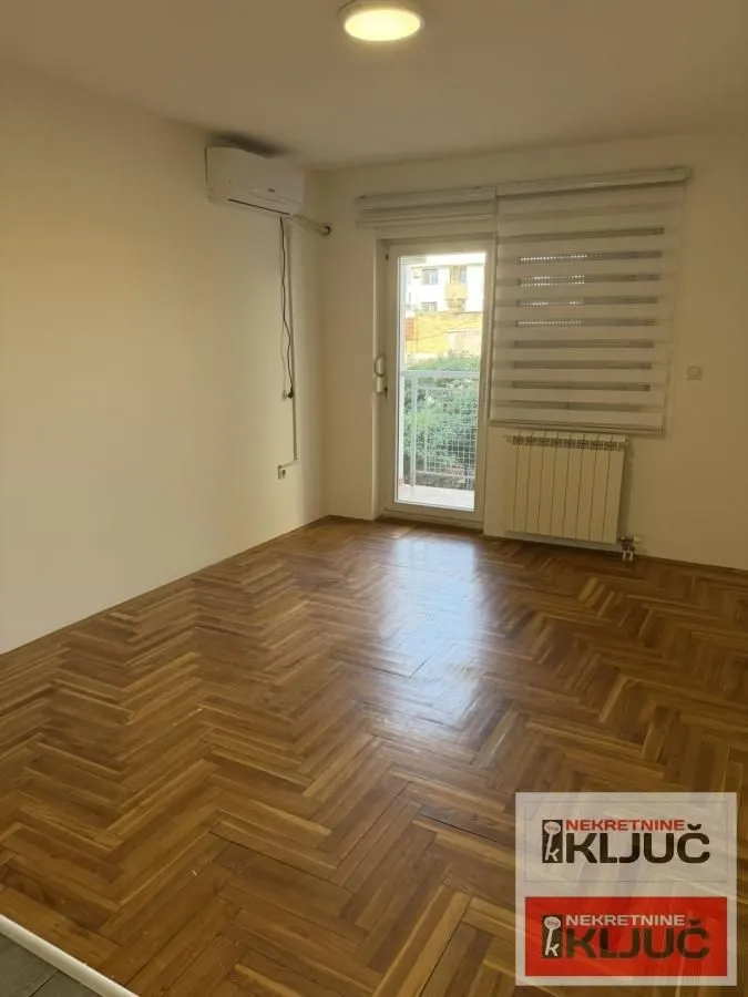 Prazna soba sa parketom, klima uređajem i izlazom na terasu.