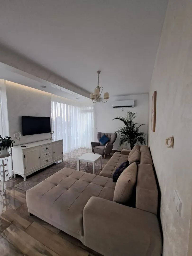 Dnevna soba sa ugaonom garniturom, TV komodom i foteljom.