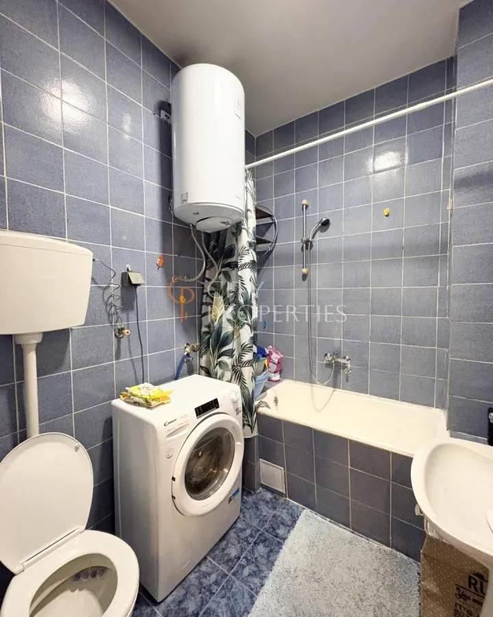 Bathroom tiled in blue with a bathtub, toilet, washing machine, and water heater.
