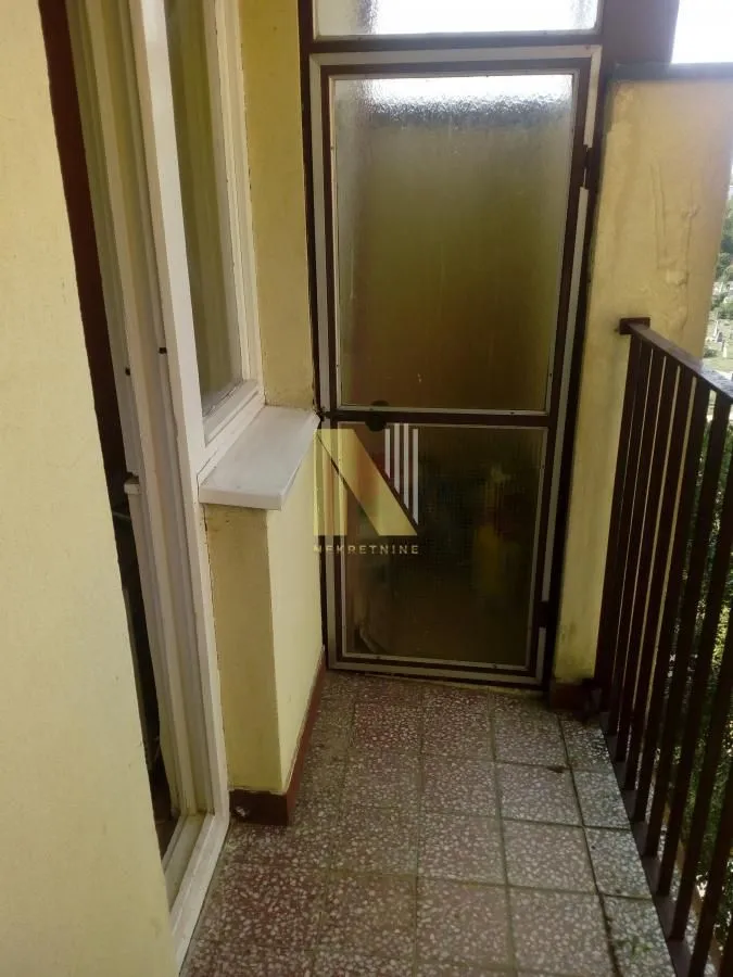 Pogled na manji natkriveni balkon sa popločanim podom i metalnom ogradom.