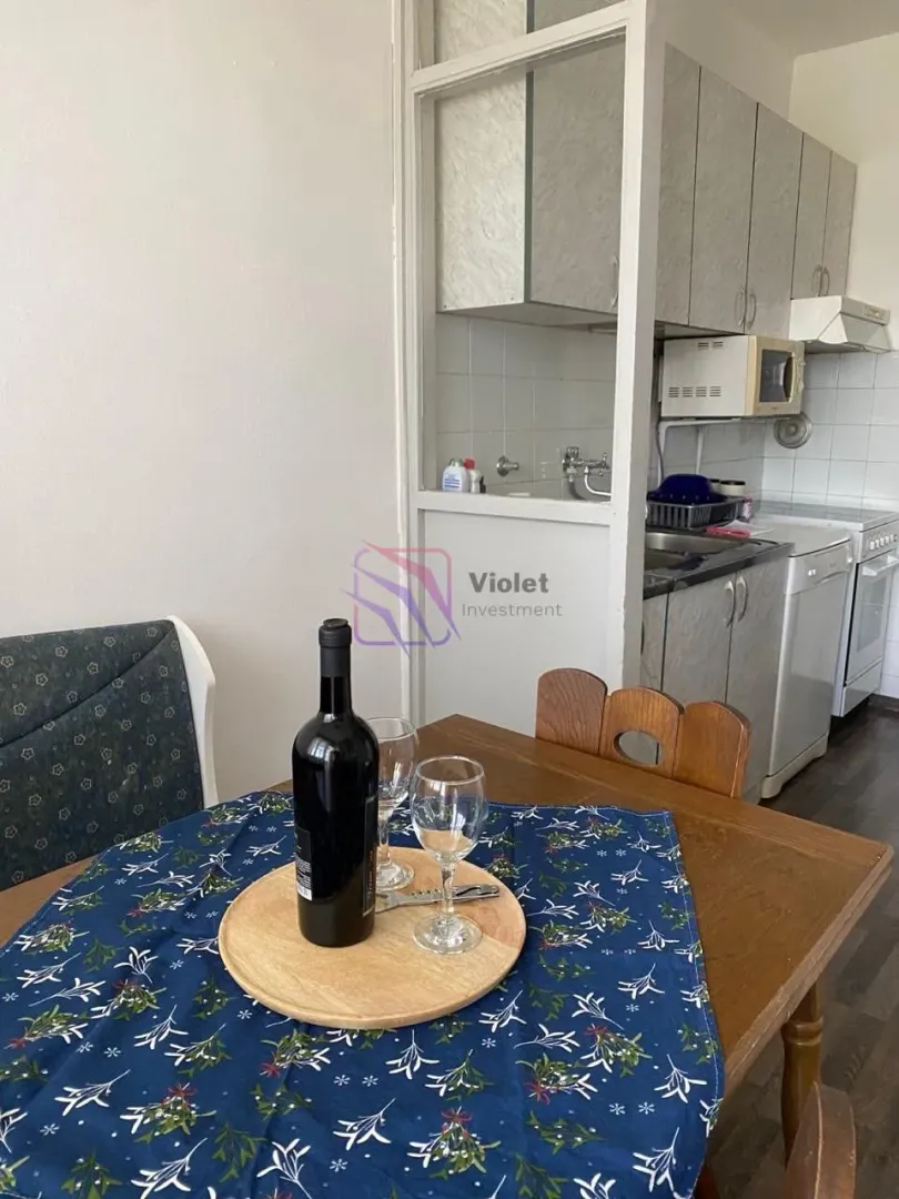 Trpezarija sa stolom i flašom vina i pogledom na kuhinju.