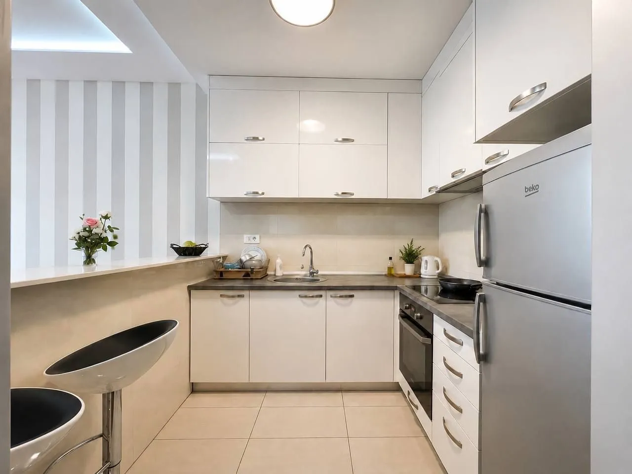 Moderna bijela kuhinja sa ugrađenim aparatima i šankom.