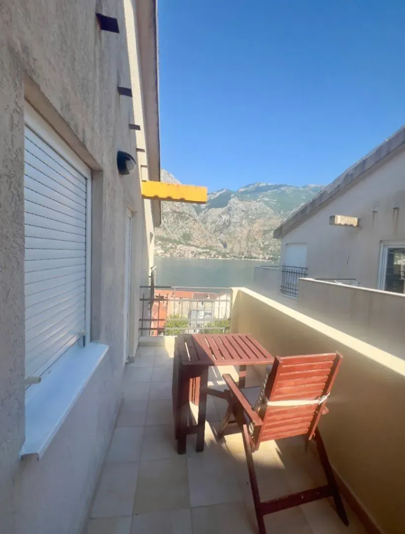 Terrace with a wooden table and chairs and a sea and mountain view.