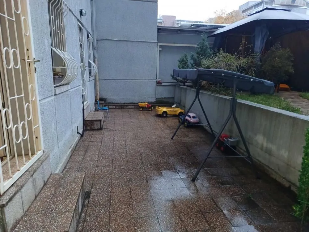 Popločano dvorište sa dečijim igračkama i ljuljaškom ispred zgrade.