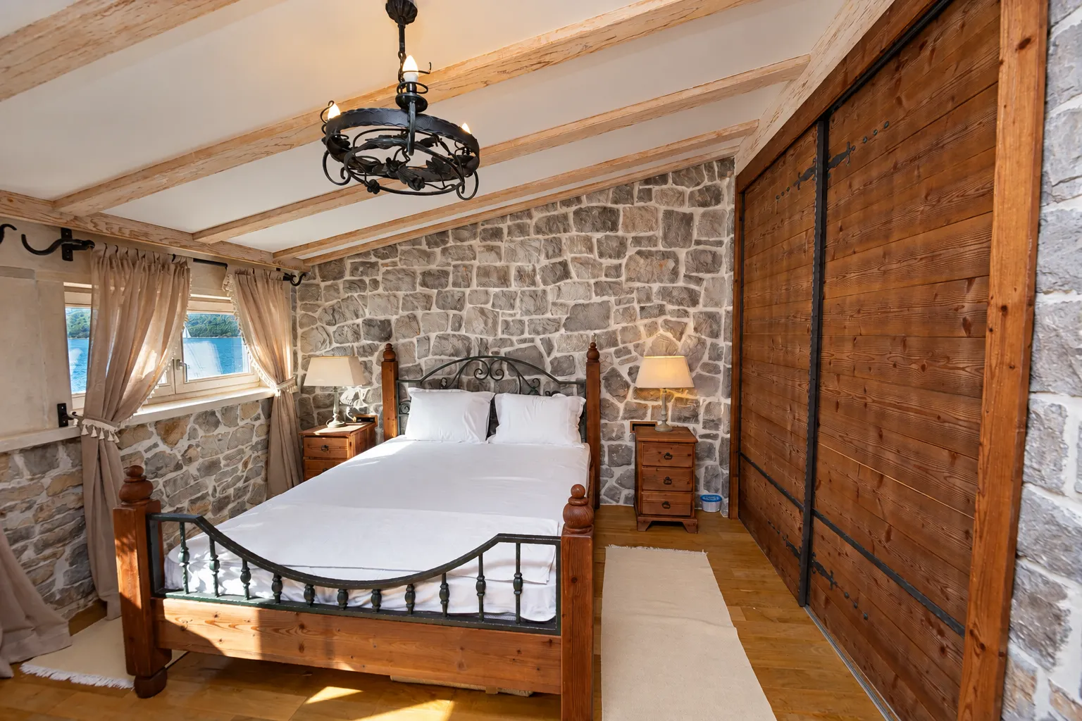 Rustic bedroom with a double bed, stone wall, and wooden beams.