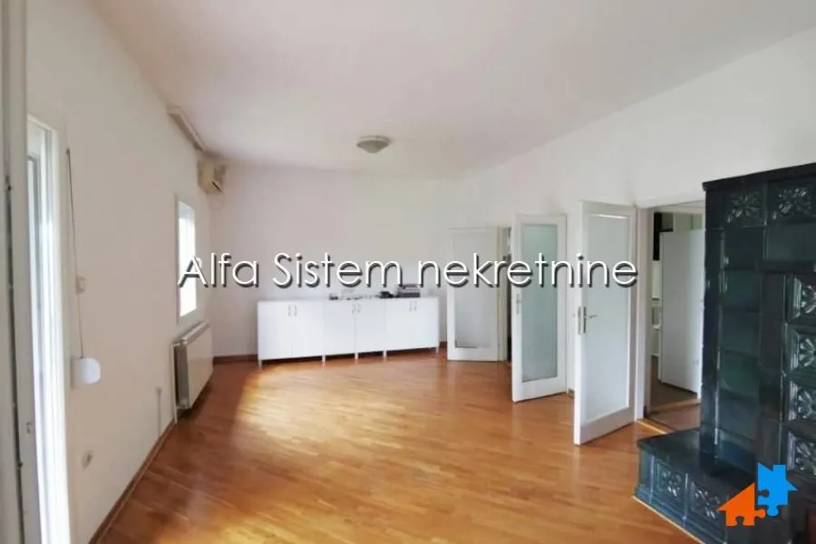 Spacious empty room with parquet flooring, white walls, and a tiled stove.