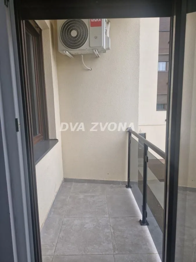 Manji popločani balkon sa klima uređajem i ogradom.