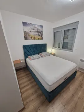 Uređena spavaća soba sa bračnim krevetom, plavim uzglavljem i prozorom. - image 2
