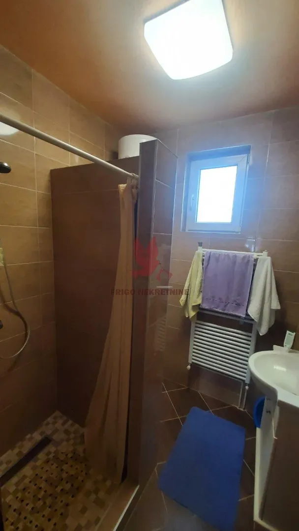 Kupatilo obloženo keramičkim pločicama sa tuš kabinom i umivaonikom.