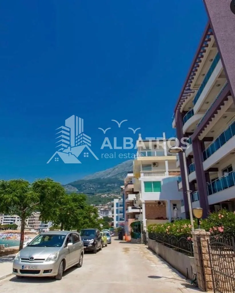 View of the street with parked cars in front of the residential building and mountains in the background.