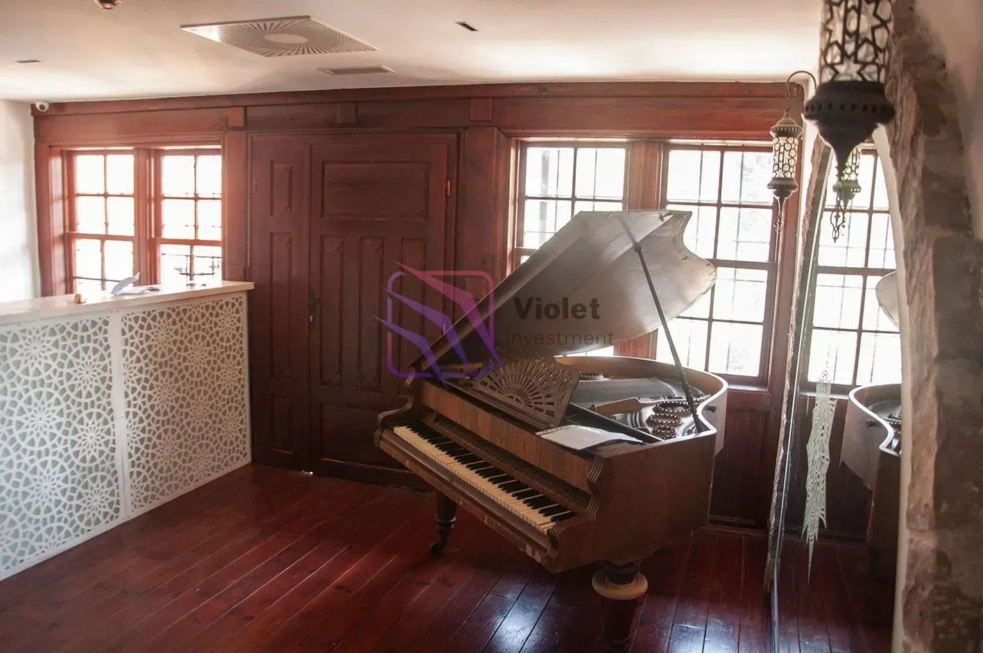 Living room with wooden flooring, a piano, and large windows.