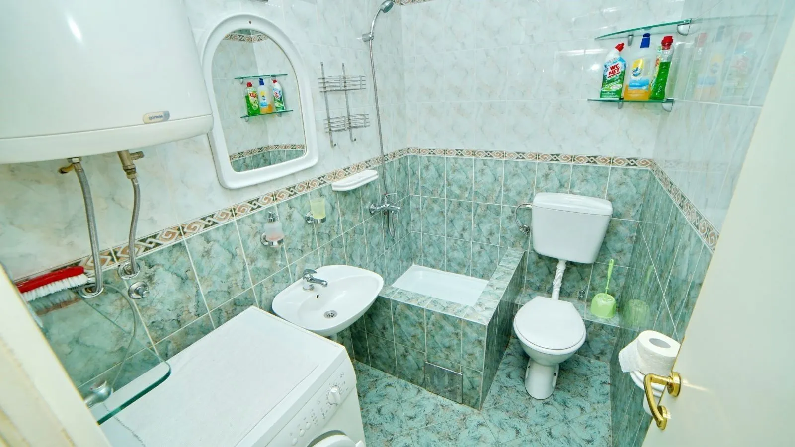 A bathroom with blue tiles, a toilet, a sink, and a washing machine.