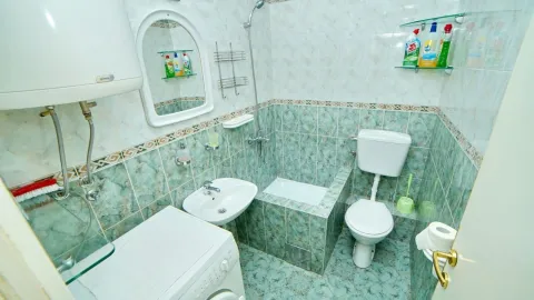 A bathroom with blue tiles, a toilet, a sink, and a washing machine. - image 10