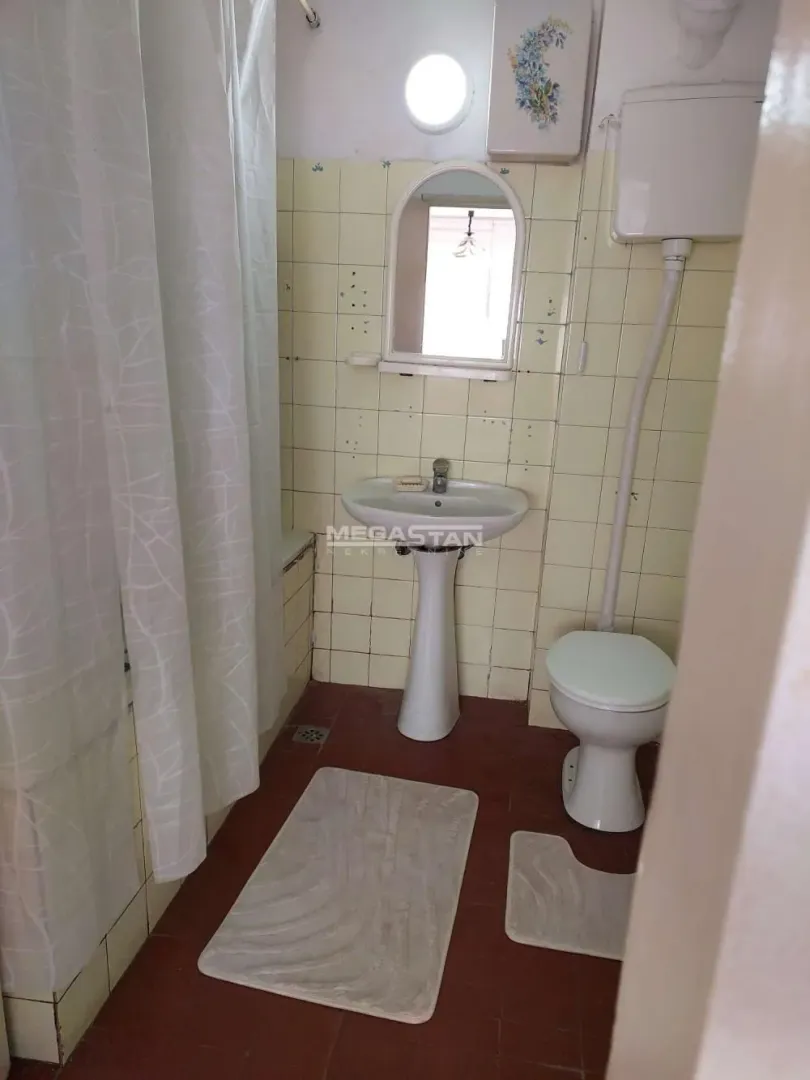 Manje kupatilo sa umivaonikom, WC šoljom i kadom sa zavesom.