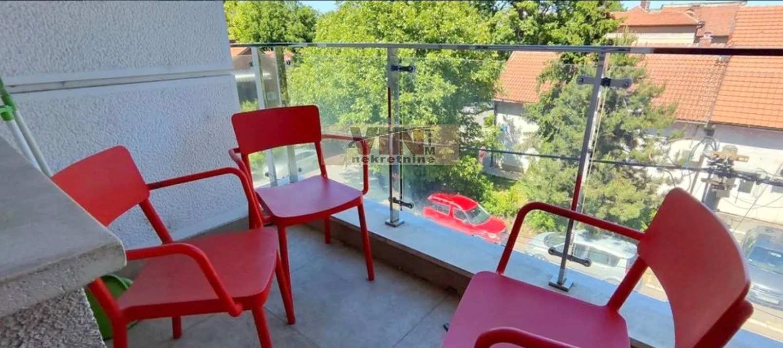 Manji namešten balkon sa staklenom ogradom i pogledom na okolinu.