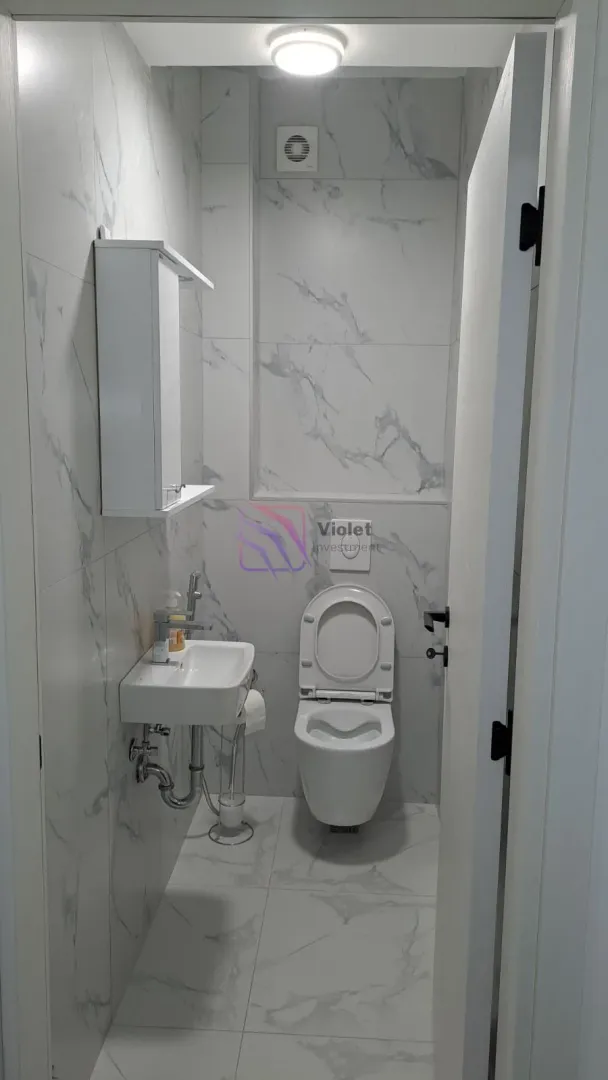 Small bathroom tiled with marble-patterned ceramic tiles, equipped with a toilet, sink, and wall cabinet.