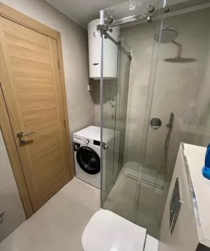 Modern equipped bathroom with a walk-in shower and washing machine. - image 7