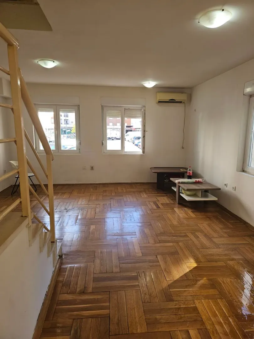 Empty living room with parquet flooring and stairs leading to the upper floor.