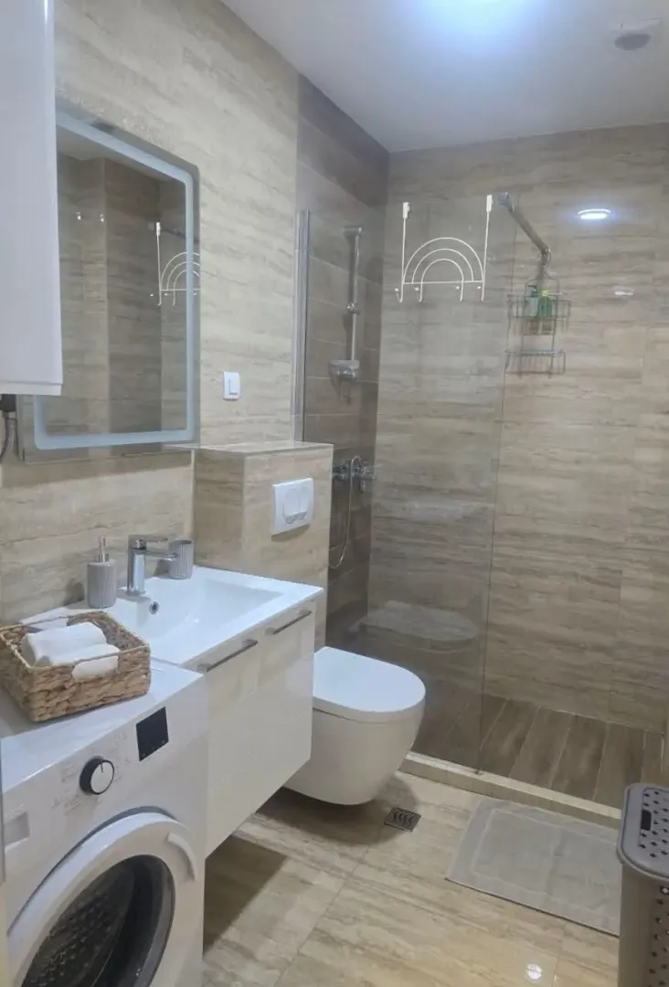 Modernly equipped bathroom with a walk-in shower, washbasin, and washing machine.