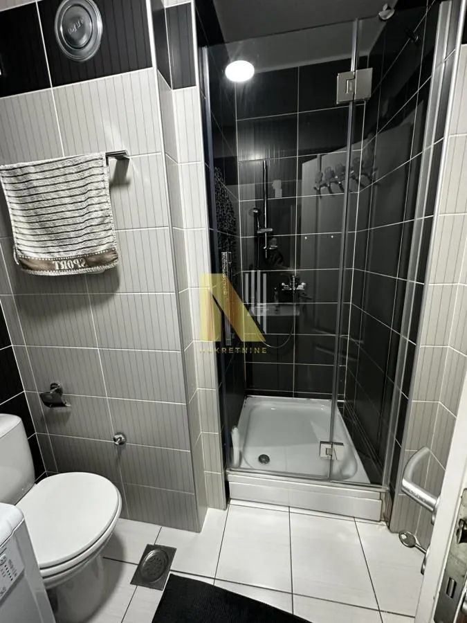 Kupatilo sa tuš kabinom, WC šoljom i belim pločicama.