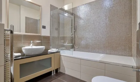 Bathroom equipped with a washbasin, bathtub with a glass screen, and mosaic tiles. - image 15