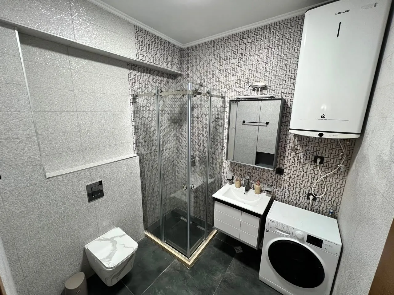 Modernly equipped bathroom with a shower cabin, washbasin, and washing machine.