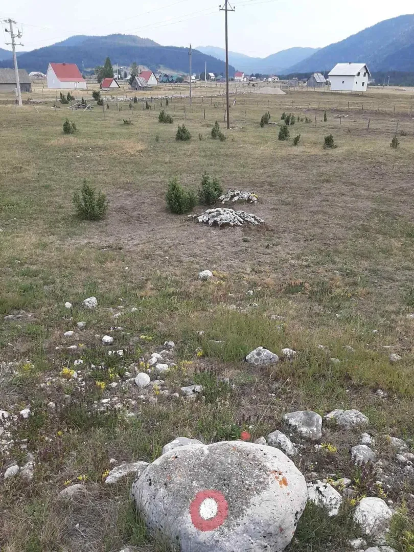 Prostrani travnati plac u planinskom predjelu sa kućama u pozadini.