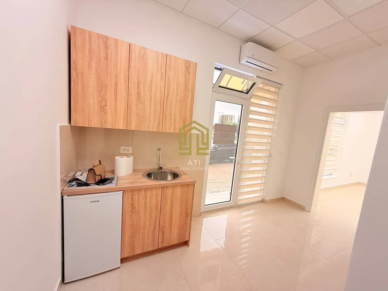 Small kitchen with wooden cabinetry and a refrigerator in a bright room.