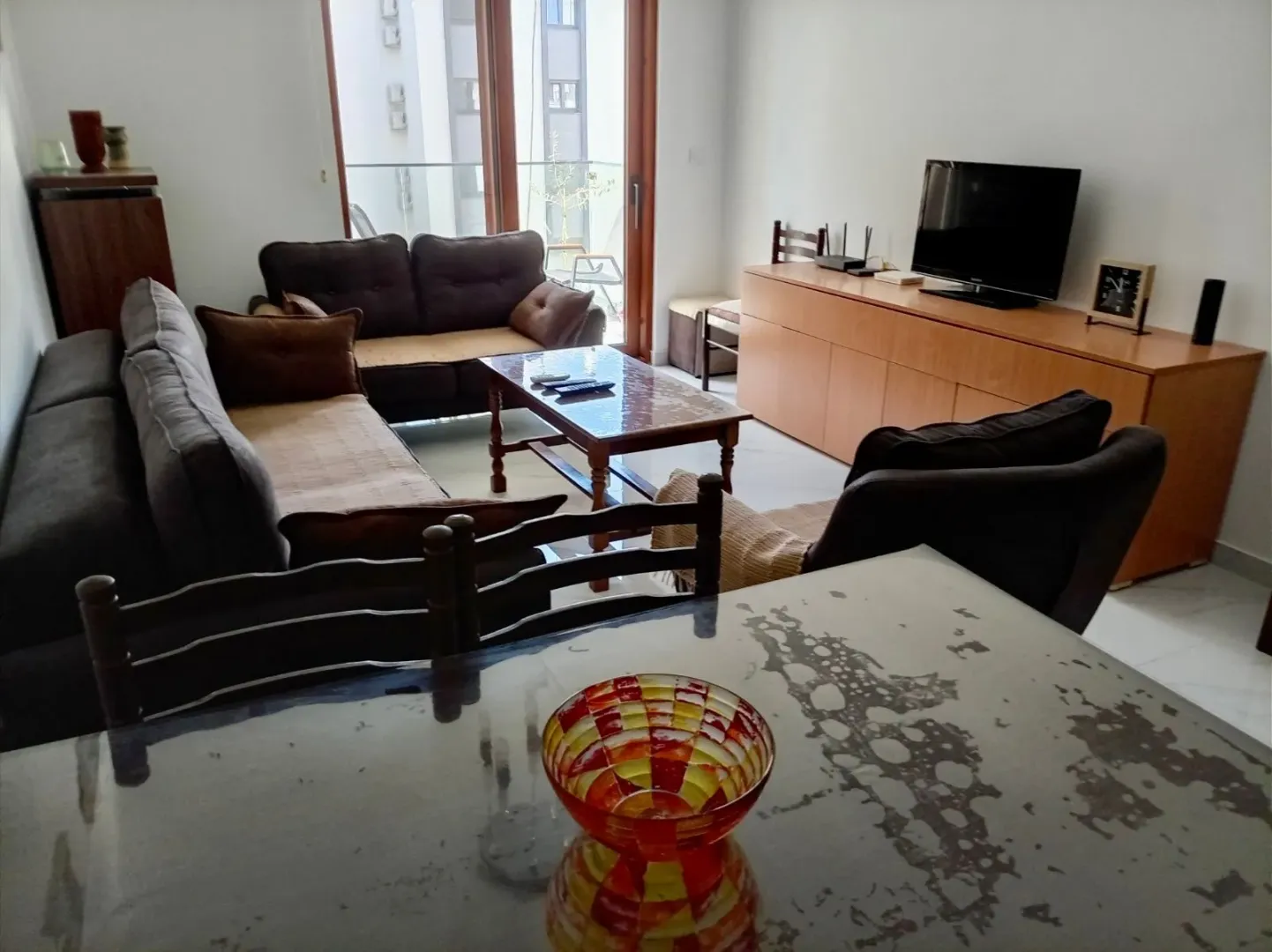 Living room with a sofa set, coffee table, television, and dining table in the foreground.