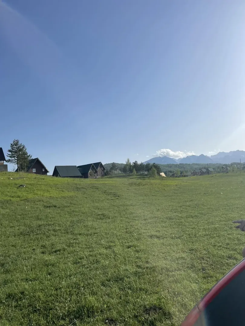 Prostrani zeleni plac sa pogledom na planine i seoske kuće u daljini.