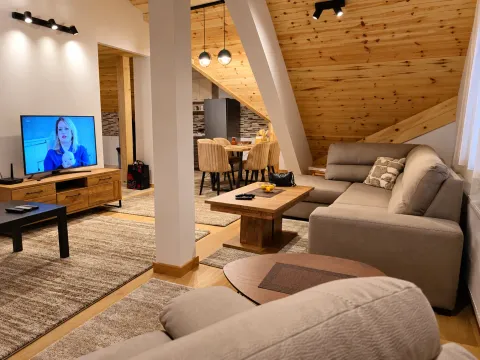 Prostrani dnevni boravak u potkrovlju sa drvenim krovnim gredama, ugaonom garniturom i TV-om. - image 5
