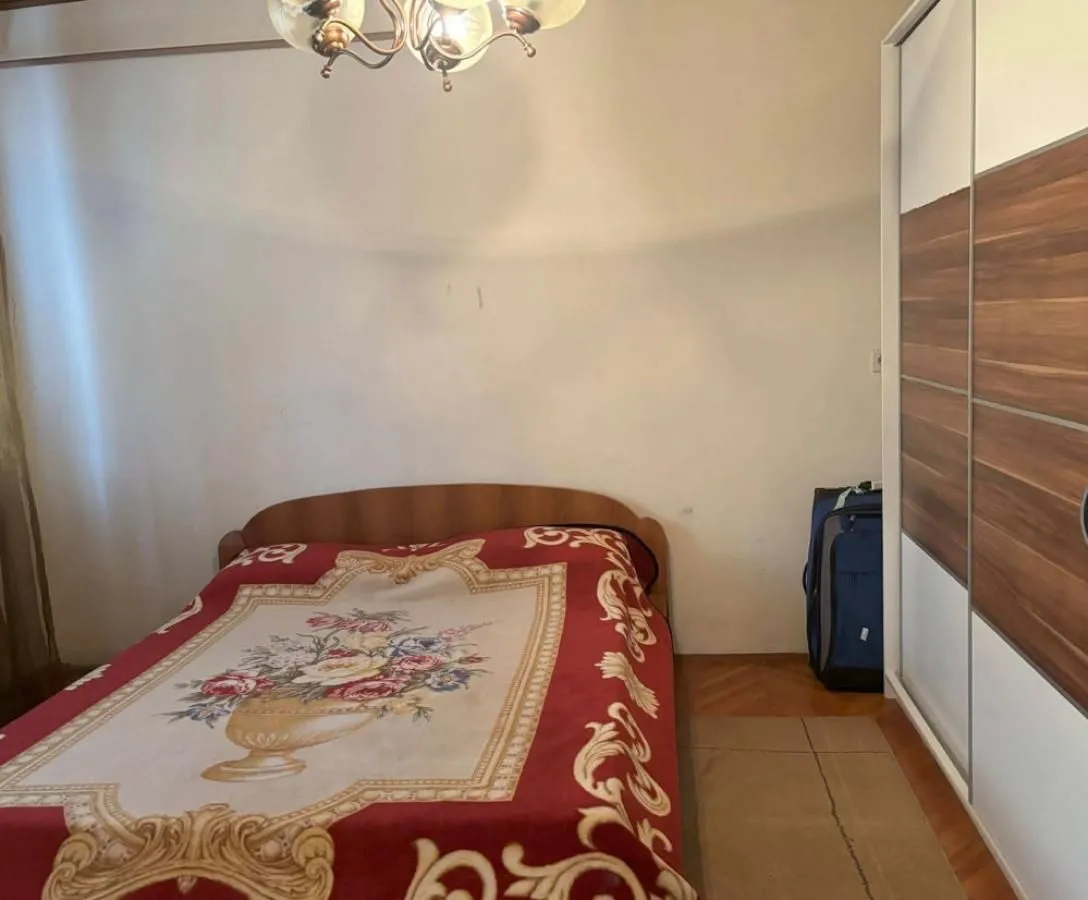 Spavaća soba sa bračnim krevetom, garderoberom i lusterom na plafonu.