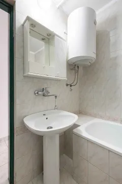 Kupatilo opremljeno umivaonikom, ogledalom, bojlerom i kadom sa pločicama na zidovima. - image 17