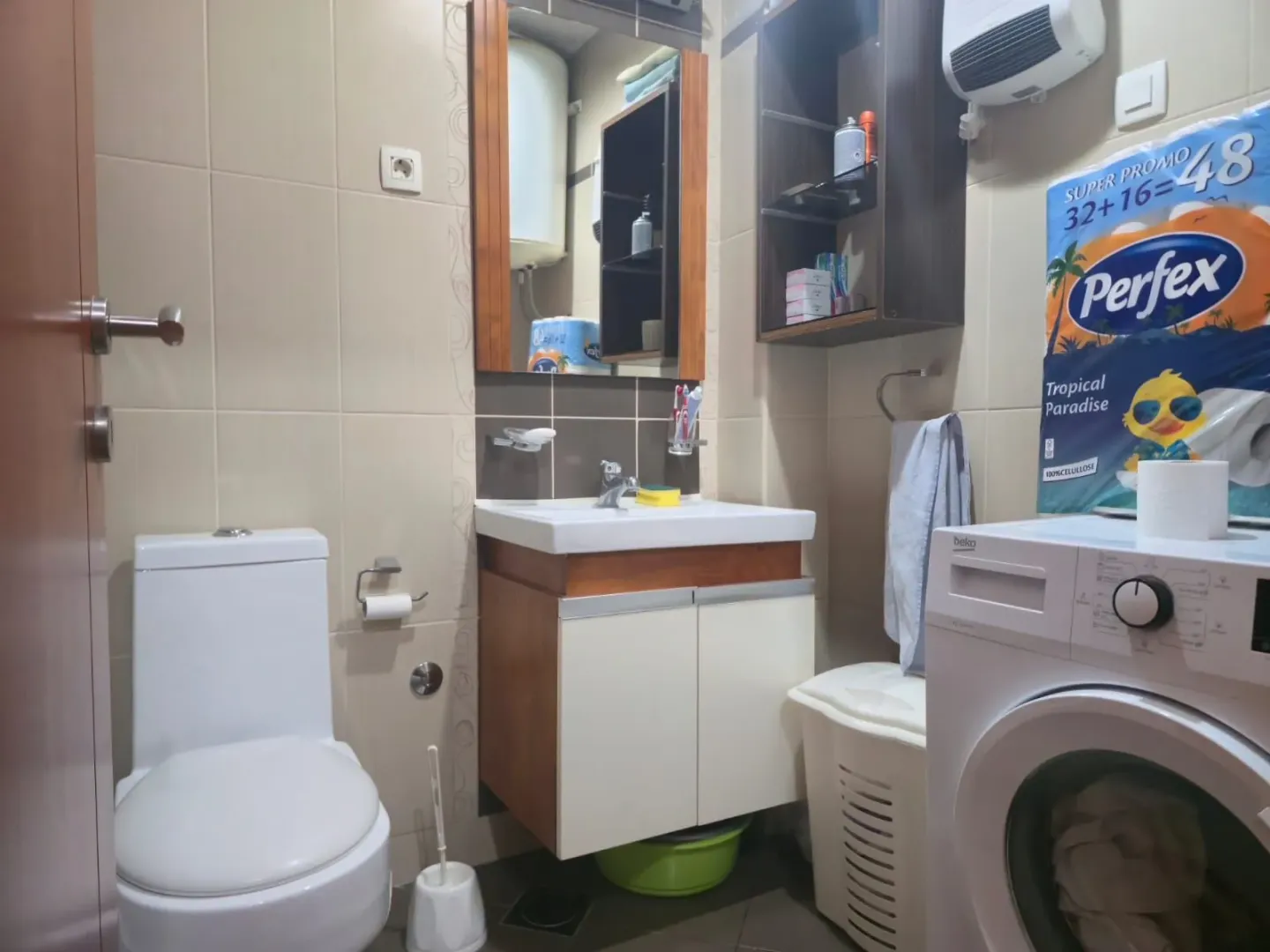 Manje kupatilo sa umivaonikom, WC šoljom, ogledalom i mašinom za veš.