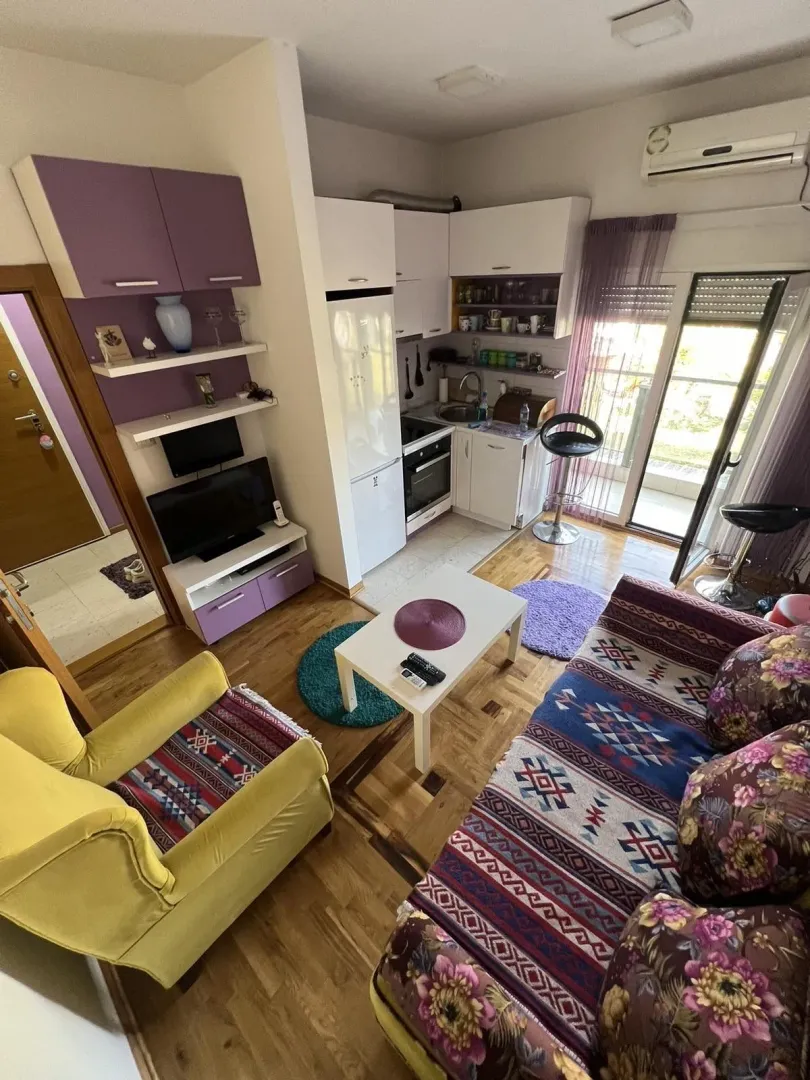 A bright living room combined with a small kitchen and balcony access.