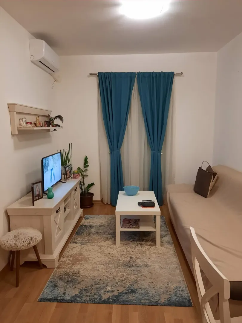 Dnevna soba sa garniturom, TV komodom i plavim zavjesama.