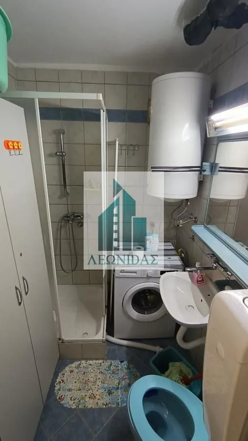 Small bathroom with a shower cabin, washbasin, toilet, and washing machine.