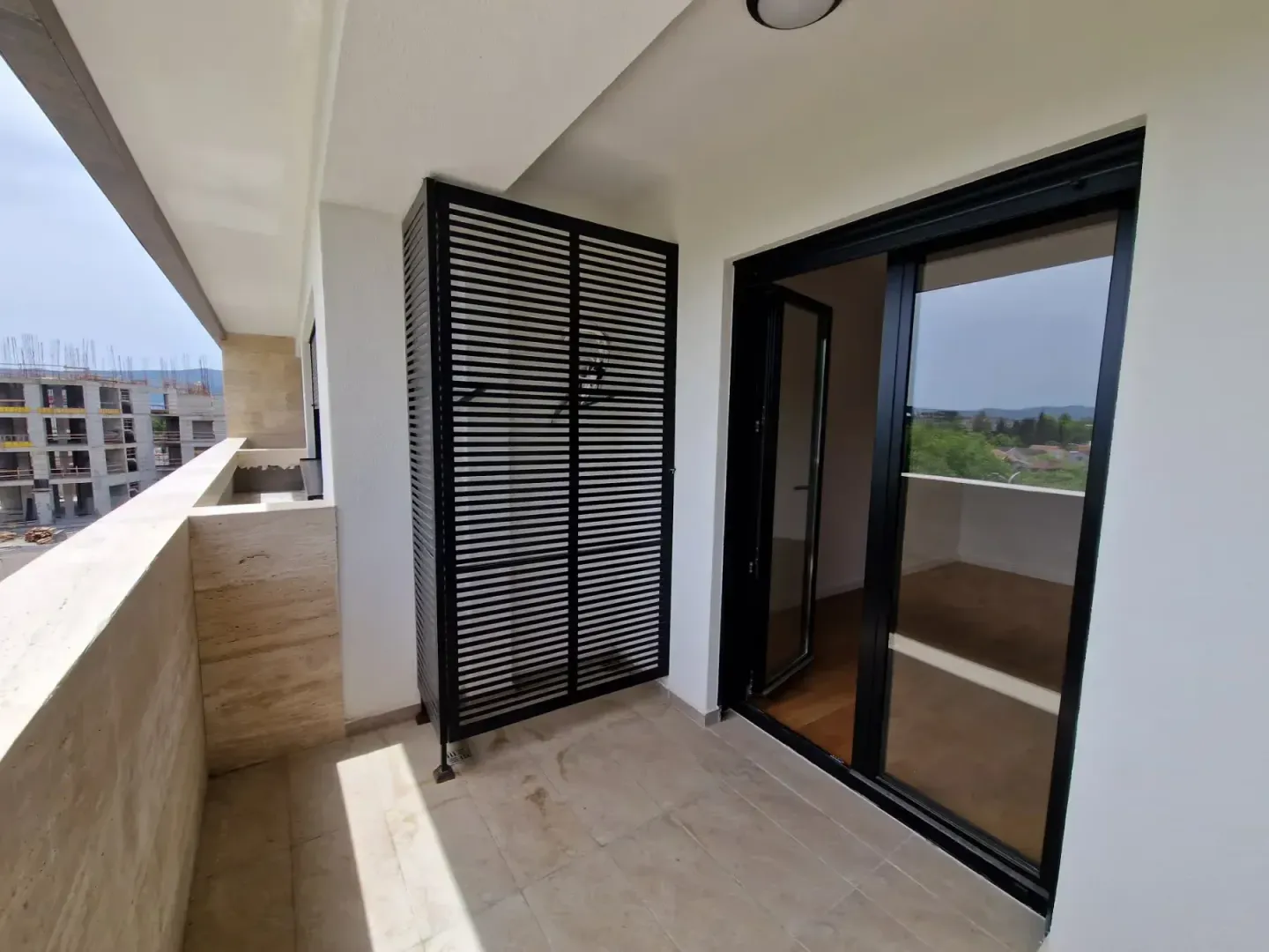 Natkriveni balkon sa pločicama i tamnim staklenim kliznim vratima.