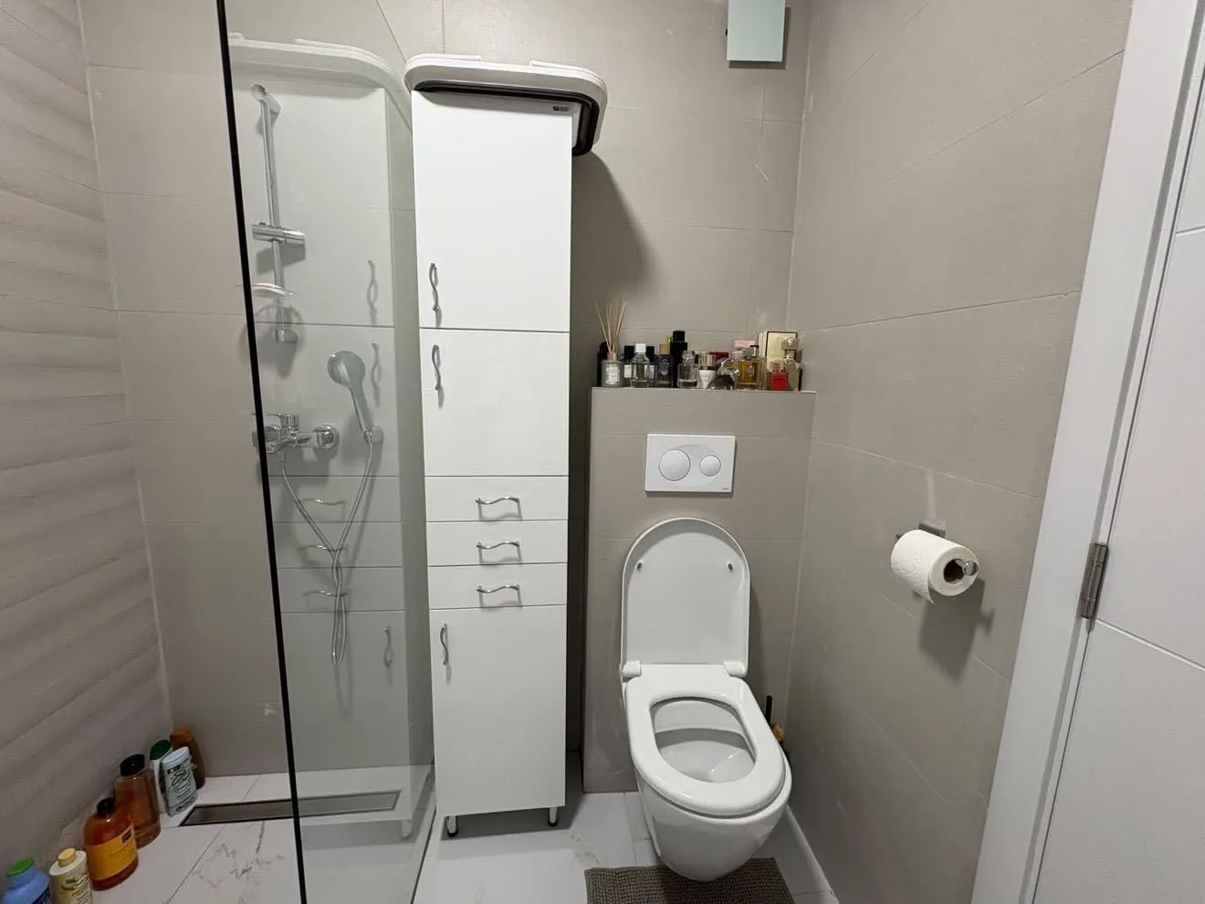 Moderne kupatilo sa tuš kabinom, WC šoljom i bijelim ormarićem.