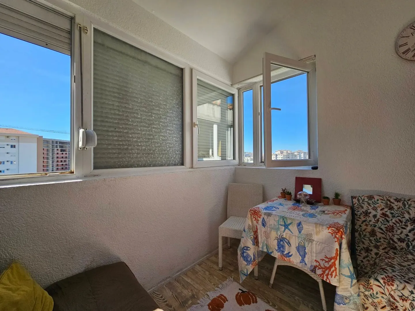 Enclosed balcony with a table, chairs, and a city view.