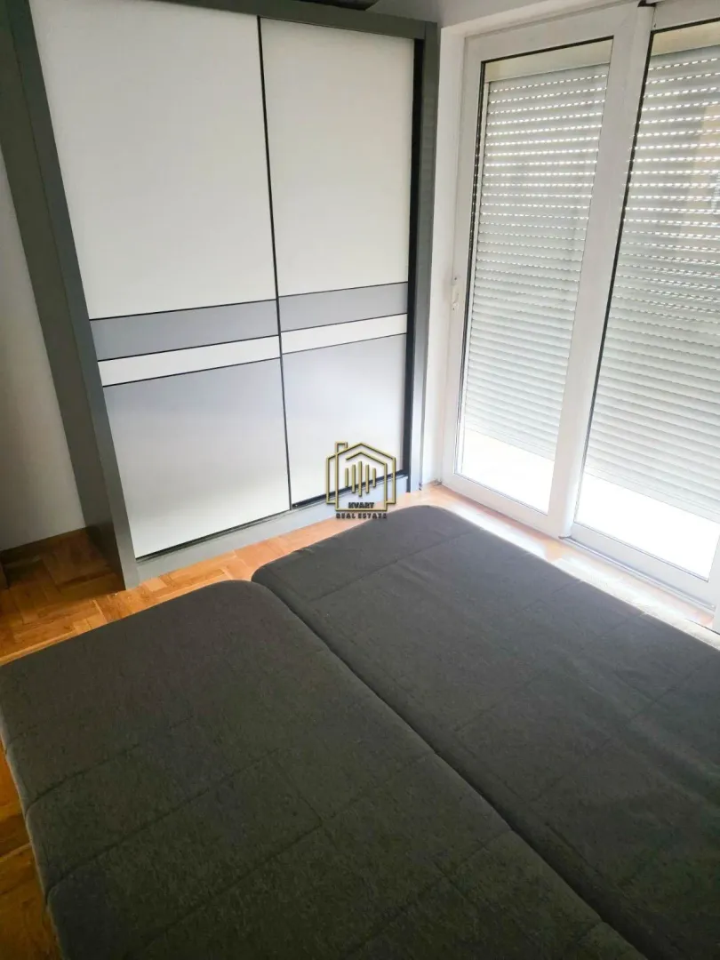 Spavaća soba sa krevetom, velikim ormarom i balkonskim vratima.