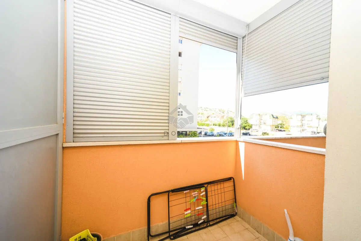 Zastakljeni balkon sa roletnama i pogledom na naselje.