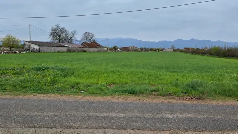 Pogled na prostranu livadu i okolne objekte sa planinama u pozadini. - image 2