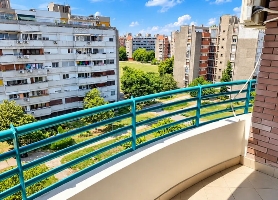 View from the balcony overlooking surrounding residential buildings and a green area.