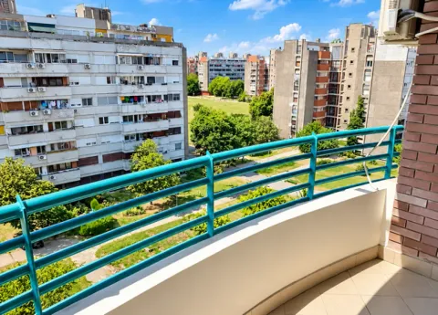 View from the balcony overlooking surrounding residential buildings and a green area. - image 13