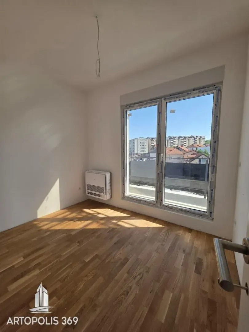 Empty room with hardwood floors and a large window overlooking the neighborhood.