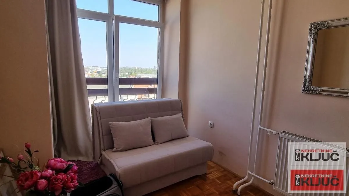 Manja dnevna soba sa kaučem, parketom i izlazom na balkon.